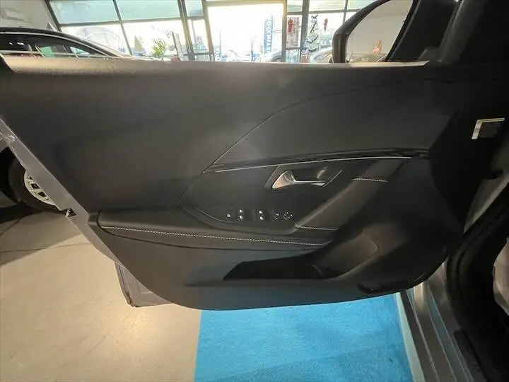 Porte côté gauche intérieure de la Peugeot 208 E-208 GT 2022 en cuir noir avec commandes de vitres et poignée argentée.