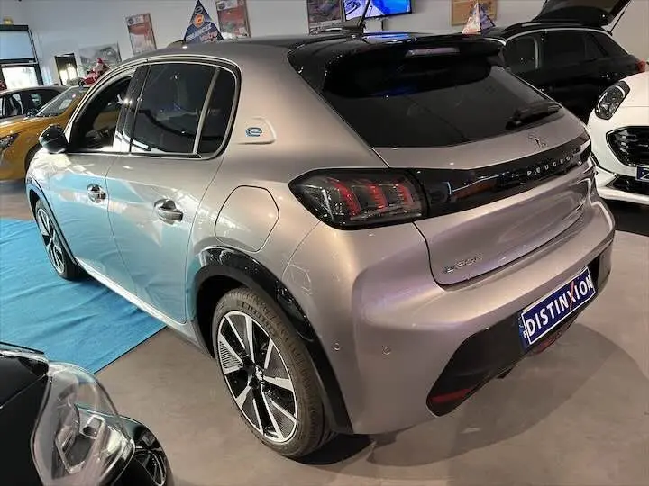 Vue 3/4 arrière droite d'une Peugeot e-208 GT électrique gris Artense avec jantes alliage et toit noir en showroom.