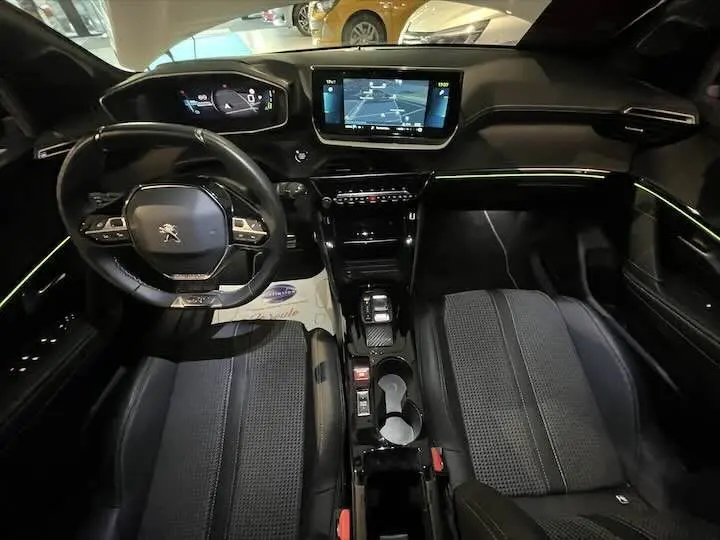 Intérieur de la Peugeot e-208 GT 2022 en gris, vue du poste de conduite avec écran central tactile et volant compact.