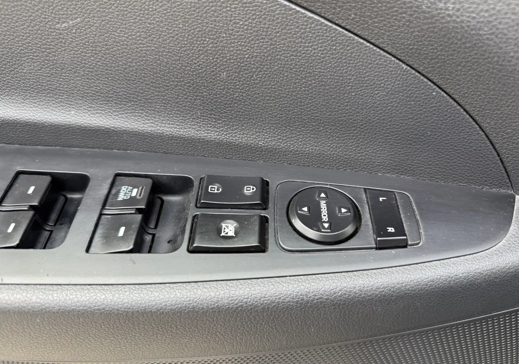 Gros plan sur les commandes de réglage des vitres et des rétroviseurs côté conducteur du Hyundai Tucson gris 2015.