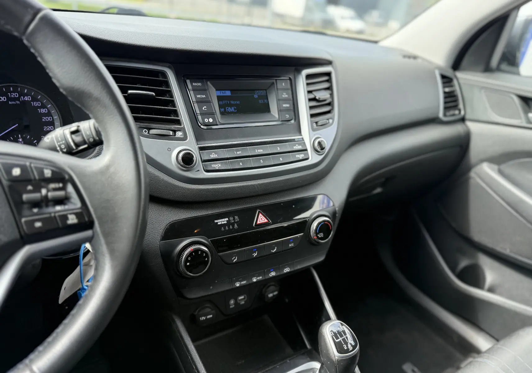 Intérieur du Hyundai Tucson 2015 gris, vue du tableau de bord côté conducteur avec console centrale et levier de vitesse manuel.