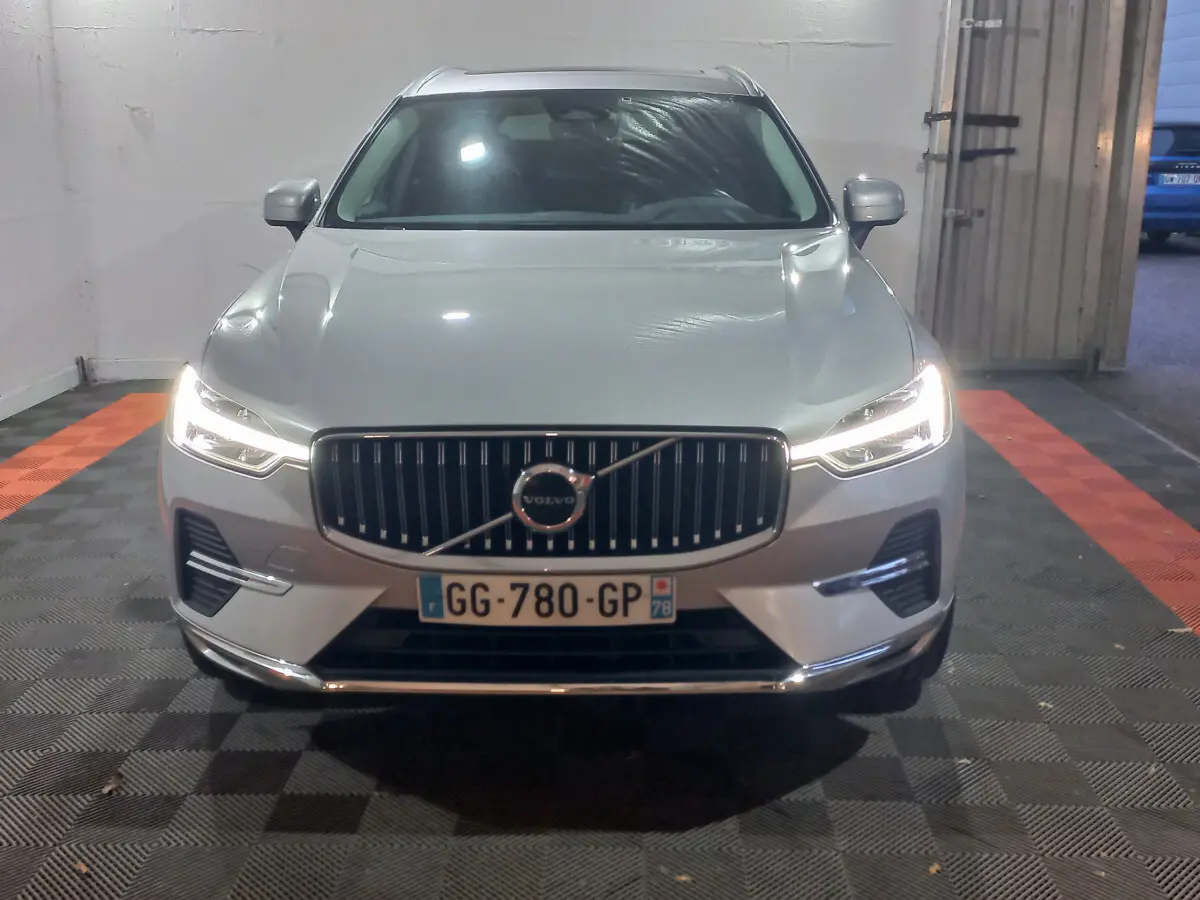 Vue frontale d'un Volvo XC60 gris clair 2022 avec phares LED allumés dans un garage fermé.
