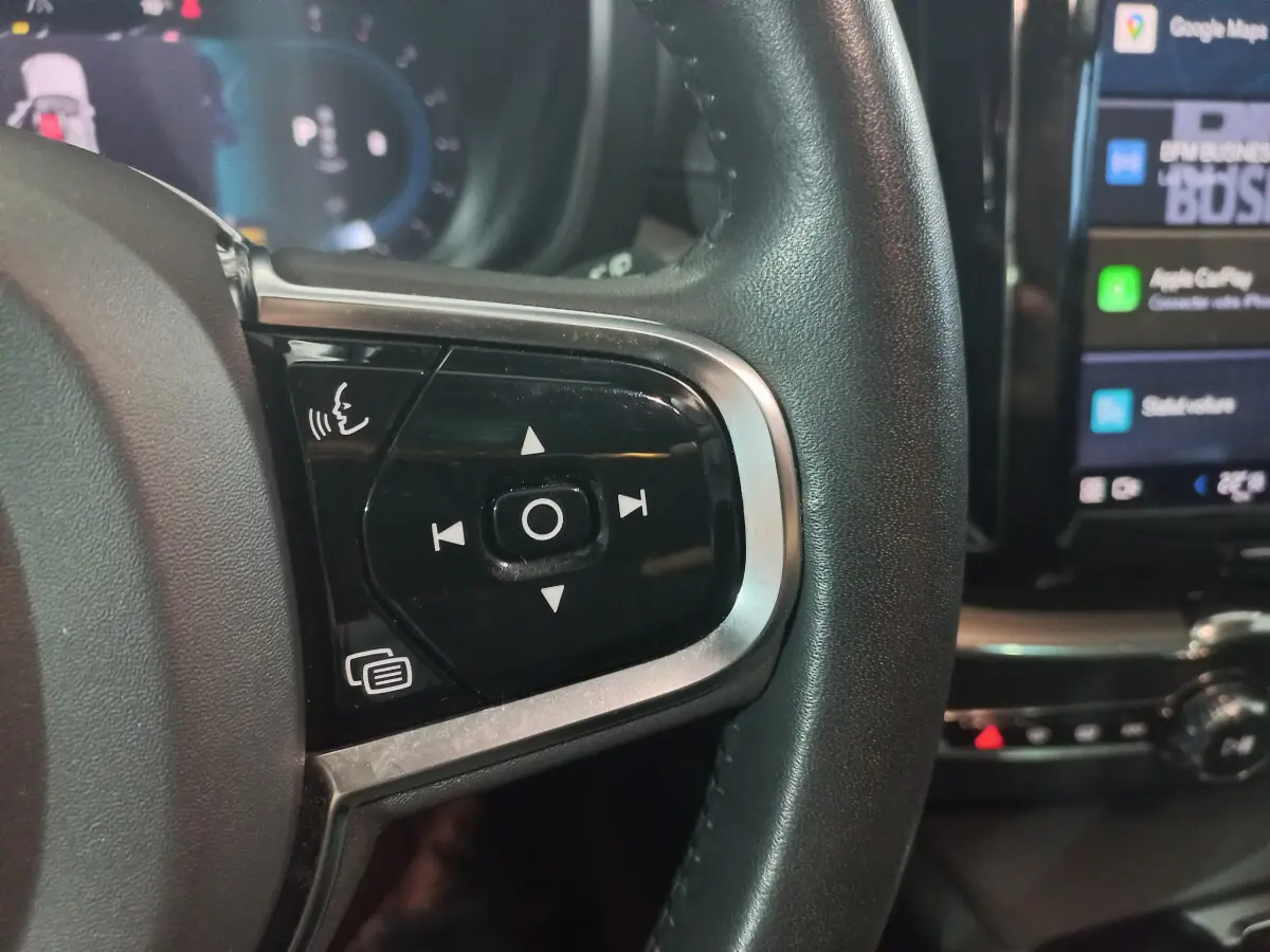 Gros plan sur les commandes vocales et multimédia à gauche du volant noir du Volvo XC60 gris clair 2022.