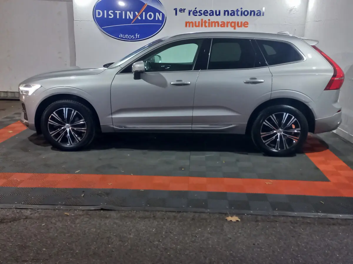 Profil côté gauche d'un Volvo XC60 gris clair 2022 garé en intérieur avec jantes noires et chromées visibles.