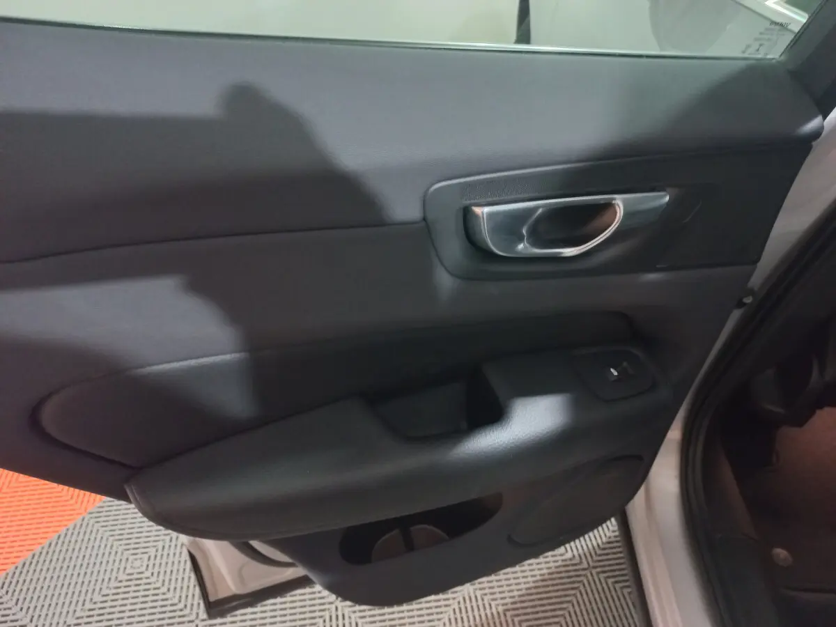 Gros plan sur la porte intérieure côté gauche du Volvo XC60 gris clair, avec poignée métal et commande de vitre.