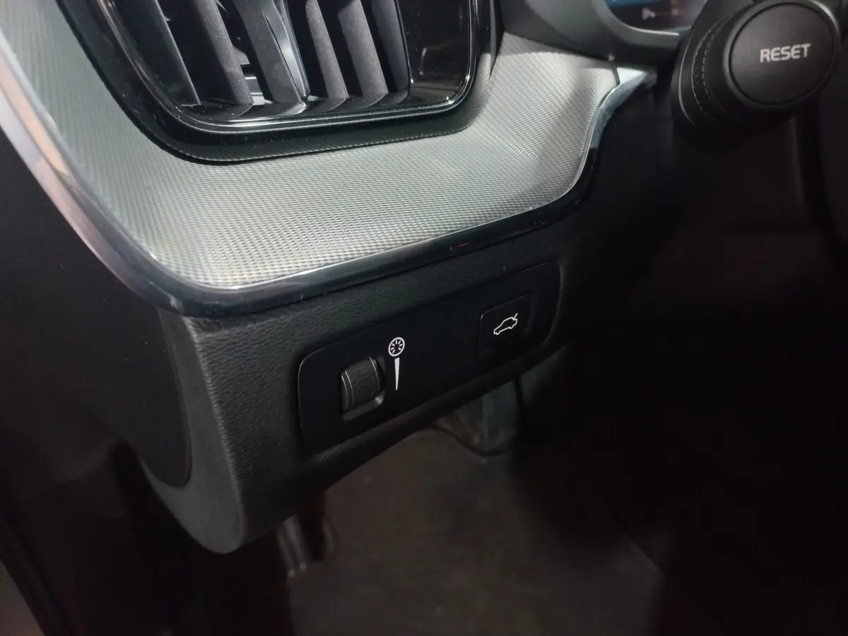 Détail du tableau de bord gris clair avec commandes d'ouverture du coffre et réglage de luminosité dans un Volvo XC60 B4 2022.