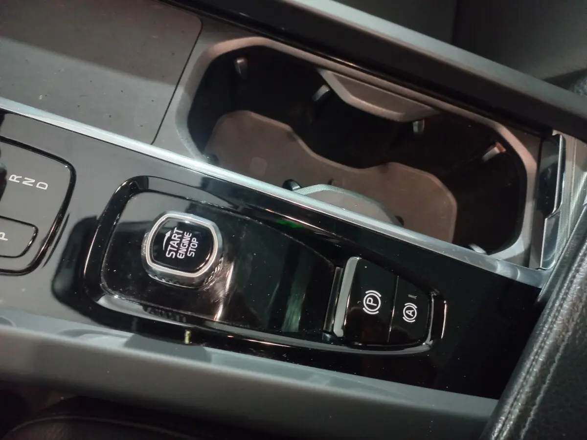 Gros plan sur la console centrale noire brillante du Volvo XC60 B4 197 Geartronic, avec bouton start/stop et commandes parking.