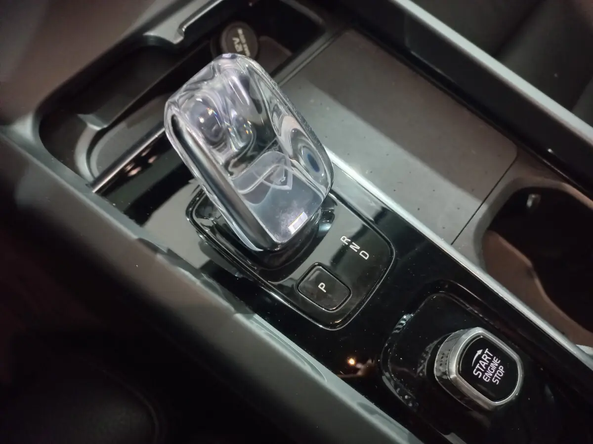 Le levier de vitesses transparent et le bouton start/stop du Volvo XC60 B4 gris clair vus en gros plan sur la console centrale.