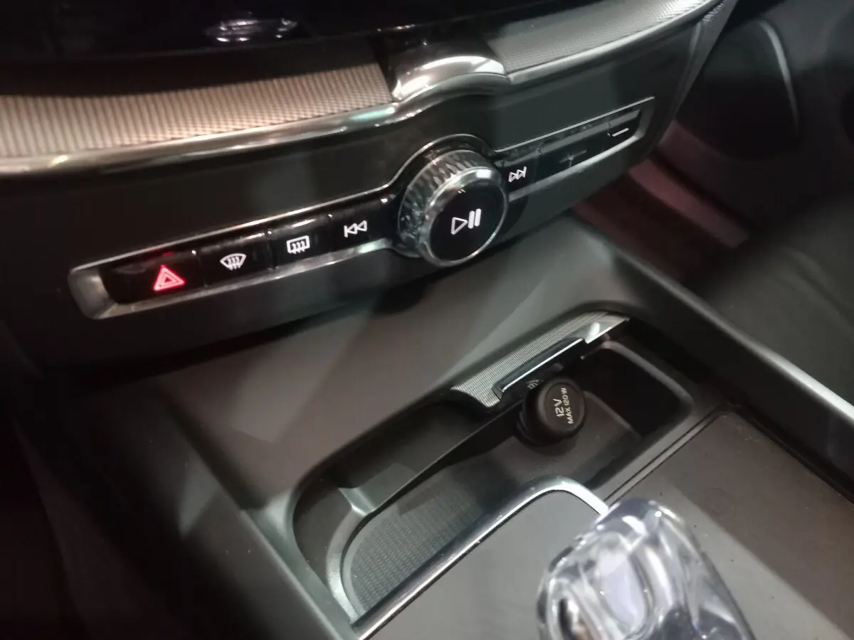 Gros plan sur la console centrale noire du Volvo XC60 B4 2022, avec bouton d'alerte rouge et prise 12V visible.