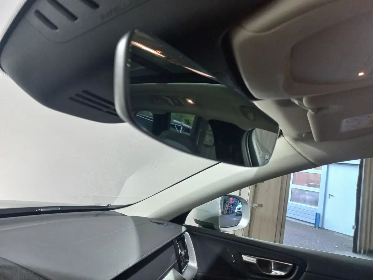 Vue intérieure du rétroviseur central et du tableau de bord noir du Volvo XC60 gris clair, côté droit visible par la fenêtre ouverte.