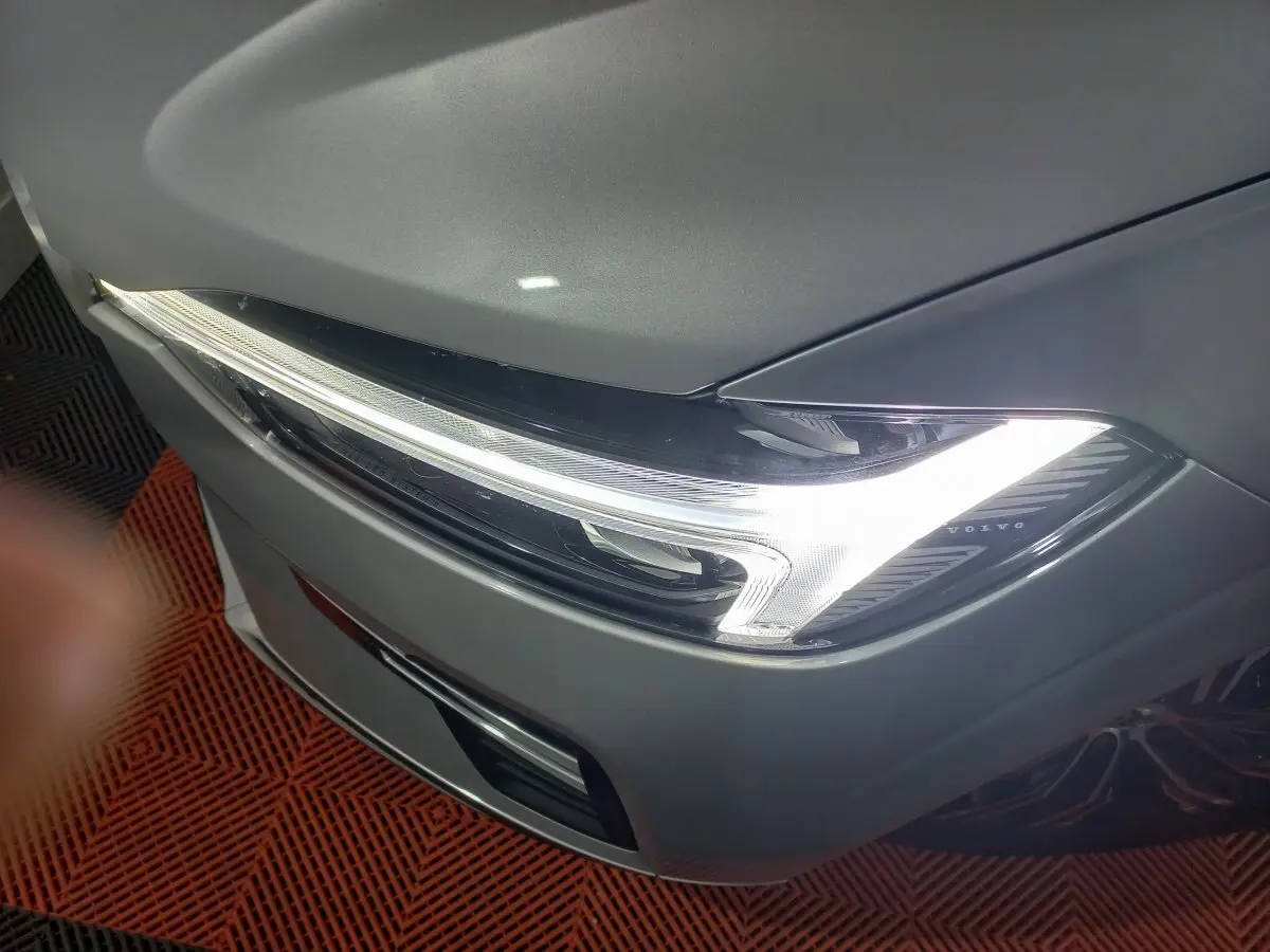 Gros plan sur le phare avant droit allumé du Volvo XC60 gris clair, soulignant son design LED distinctif.