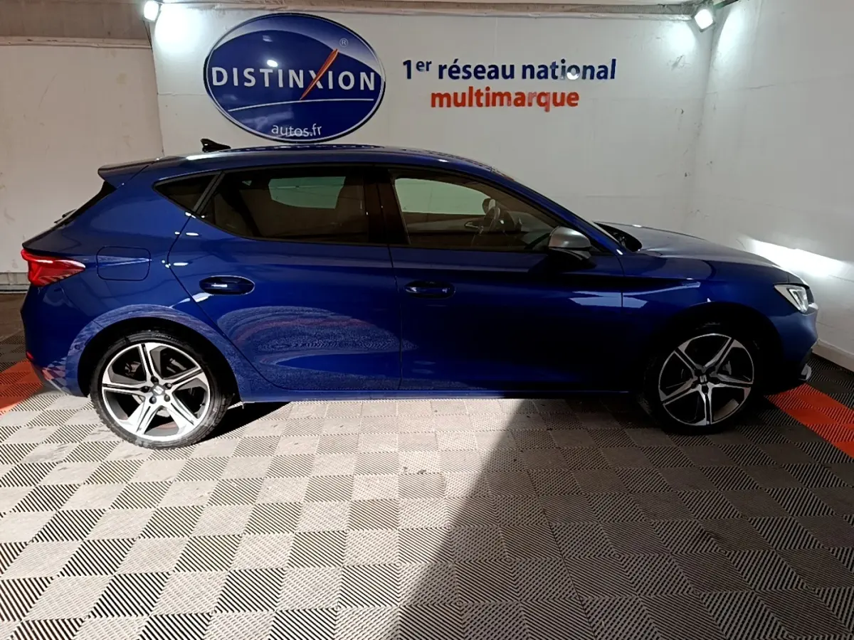 Vue de profil côté gauche d'une SEAT Leon bleu 2021 dans un showroom avec jantes alliage et vitres teintées.