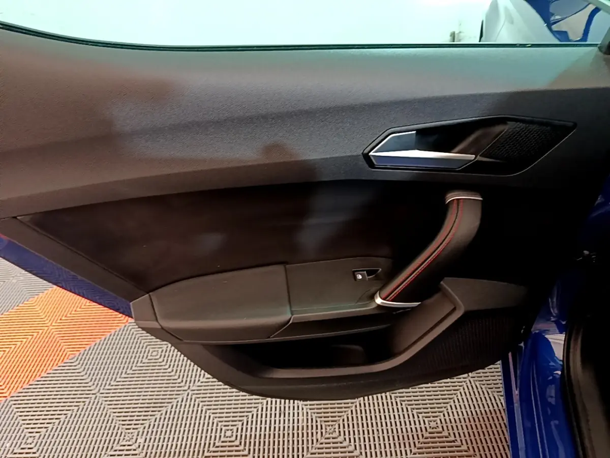 Intérieur côté gauche de la porte avant d’une SEAT Leon bleu, avec poignée noire et surpiqûres rouges.