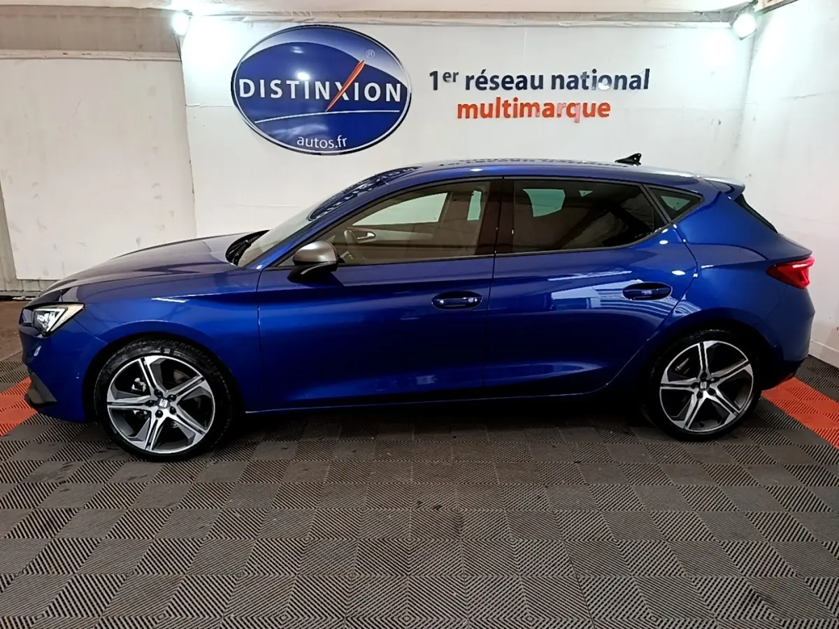 Vue de profil côté gauche d'une SEAT Leon bleu 2021 avec jantes alliage et rétroviseurs argentés dans un showroom.