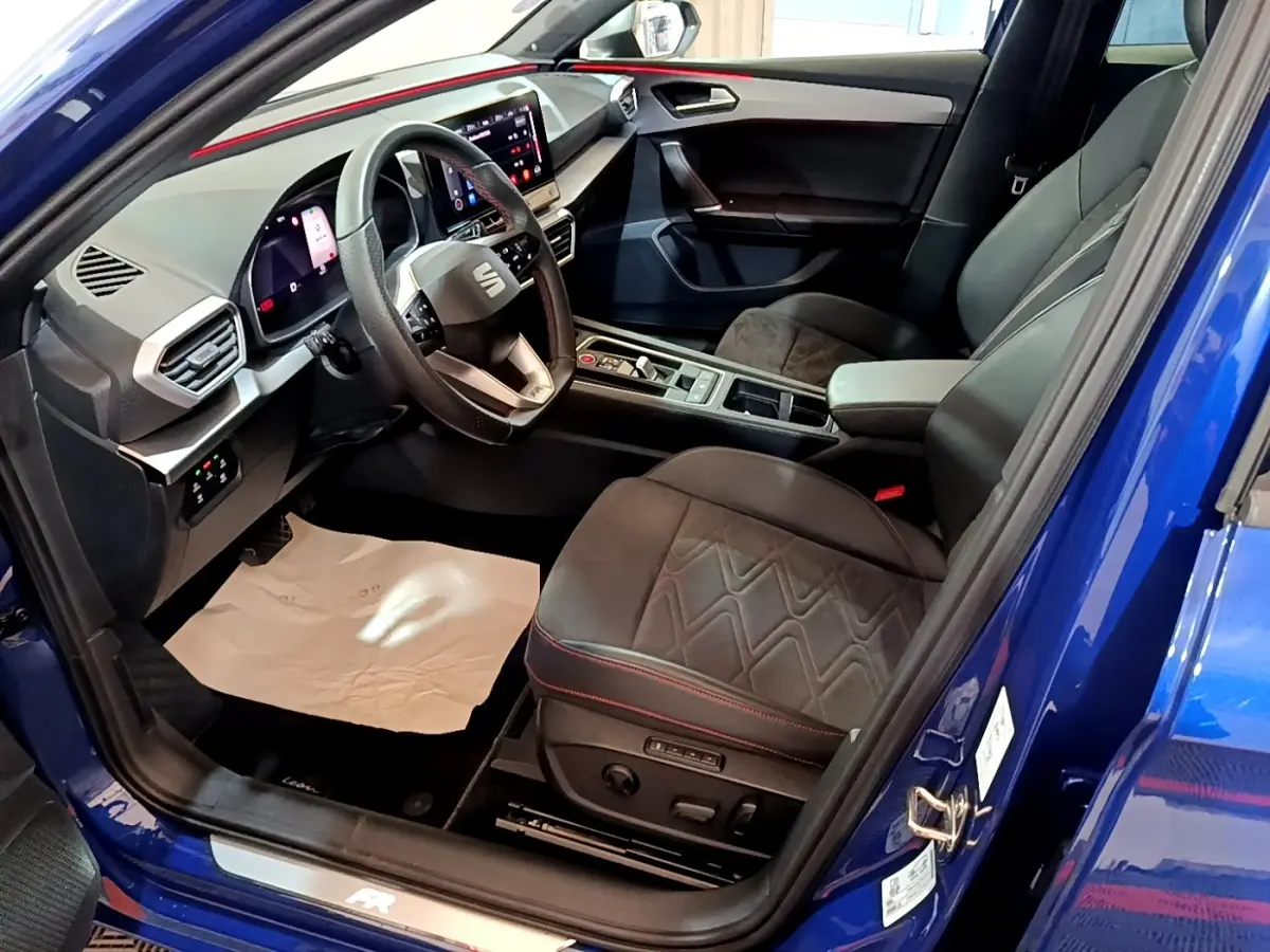 Vue intérieure côté conducteur d’une SEAT Leon bleu 2021, avec sièges noirs et tableau de bord digital lumineux.