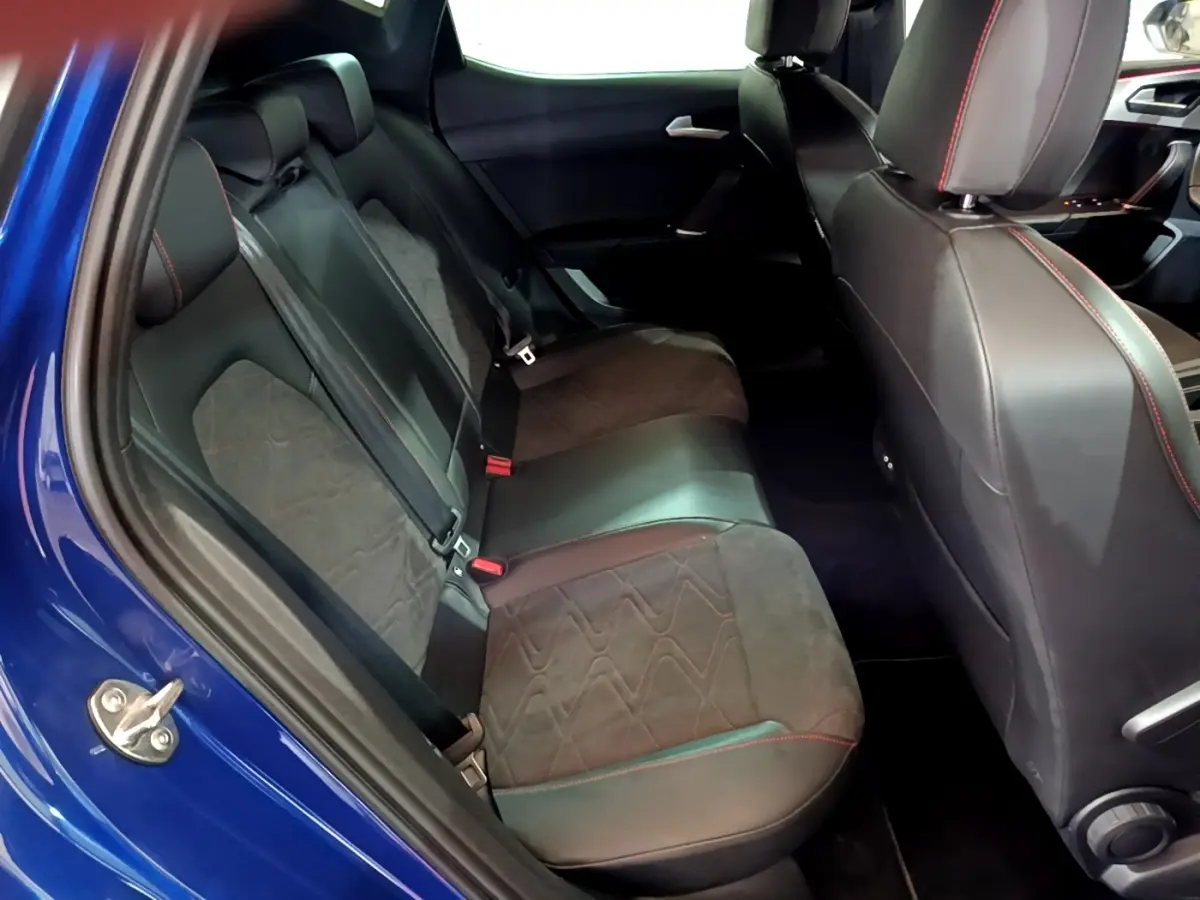 Vue intérieure côté gauche des sièges arrière en cuir noir avec surpiqûres rouges d'une SEAT Leon bleu 2021.