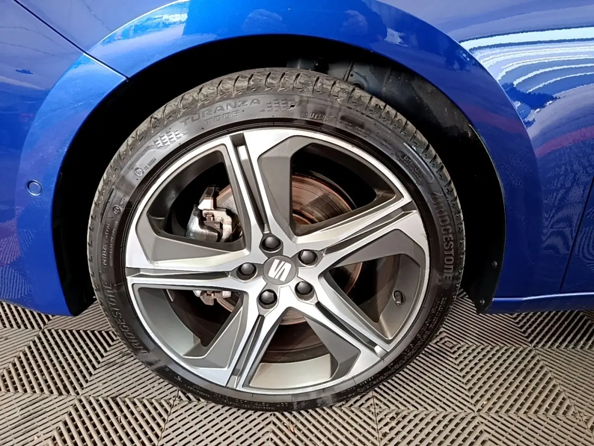 Gros plan sur la roue avant gauche d'une SEAT Leon bleu 2021, mettant en valeur l'aile et le pneu Bridgestone.