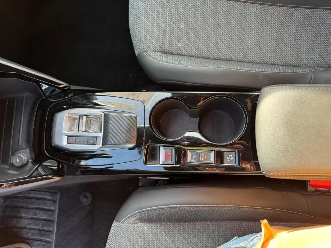 Vue plongeante sur la console centrale noire du Peugeot 2008 Hybrid 136 avec boutons frein à main et mode drive hold.