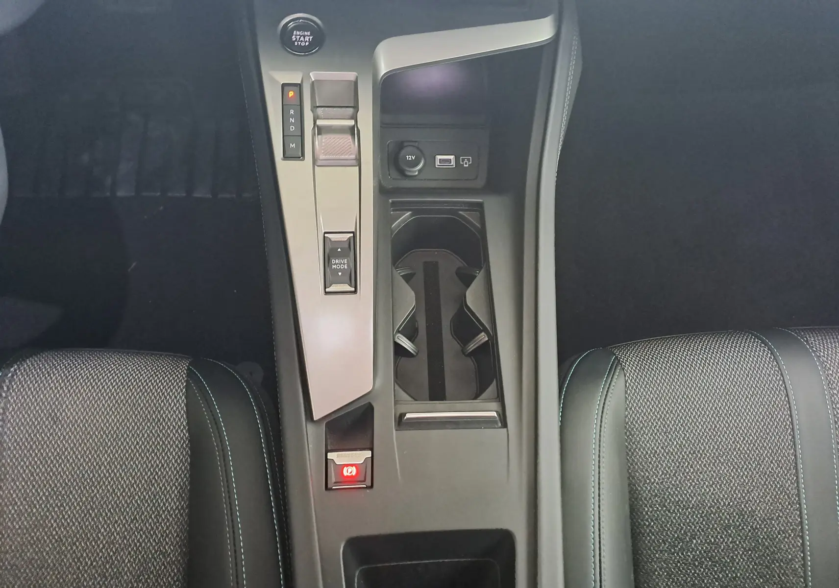 Vue plongeante sur la console centrale grise de la Peugeot 308 2023 avec levier de boîte auto et porte-gobelets entre sièges noirs.