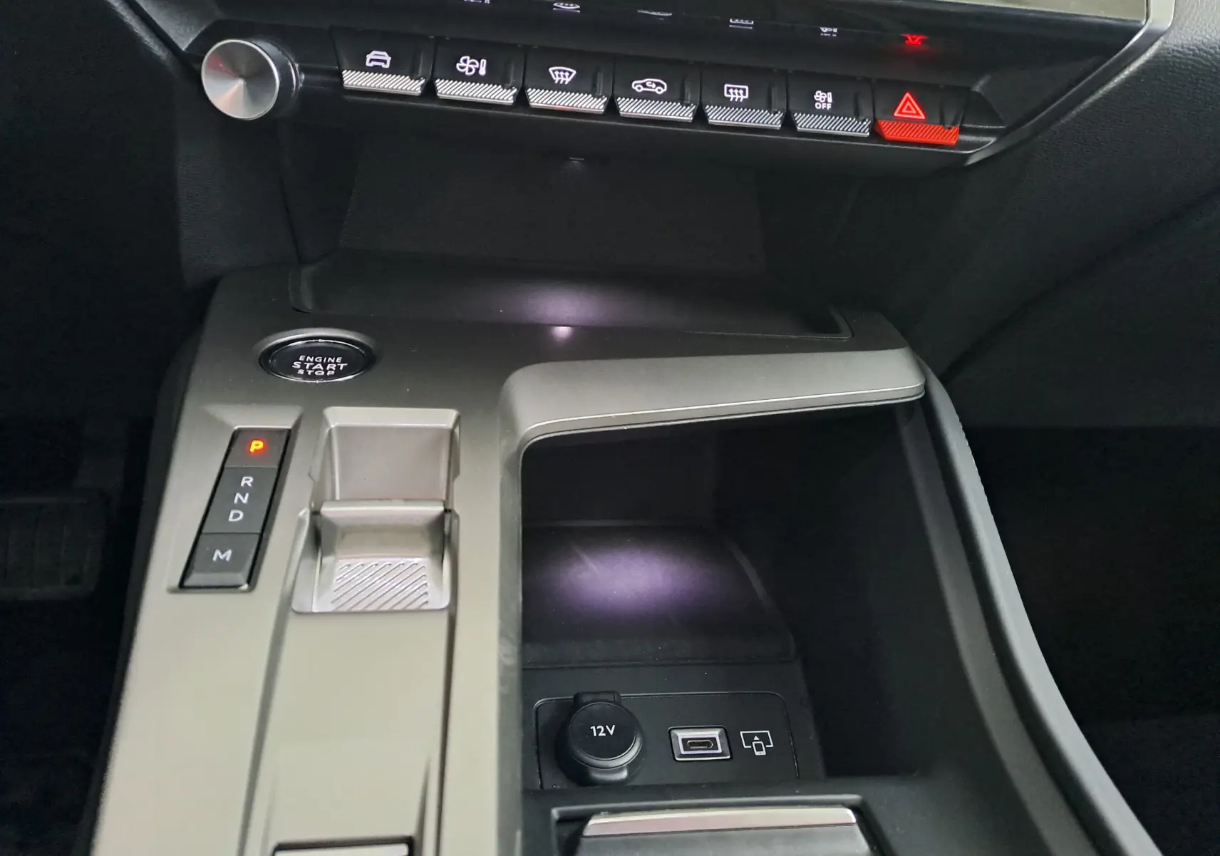 Vue rapprochée de la console centrale grise de la Peugeot 308 2023 avec bouton start, sélecteur de boîte auto et prises USB et 12V.