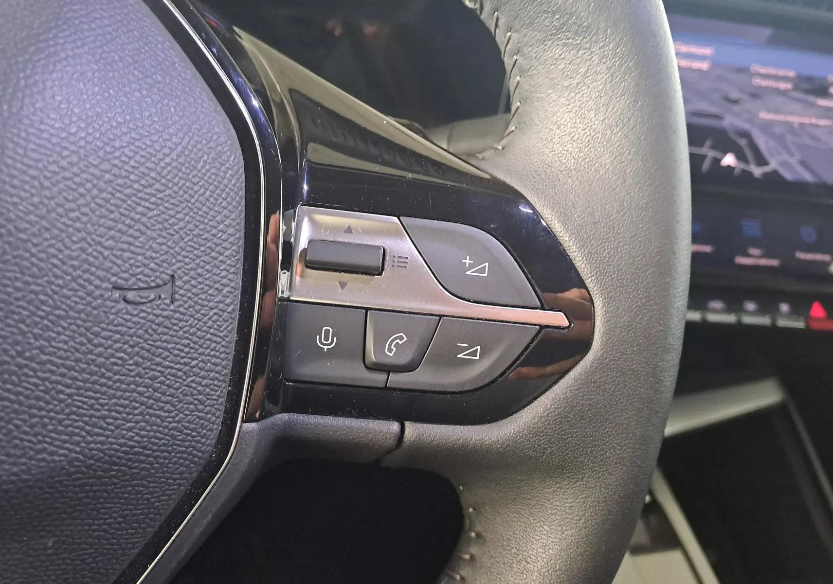 Gros plan sur les commandes gauche du volant cuir gris d'une Peugeot 308 2023 avec écran tactile en arrière-plan.