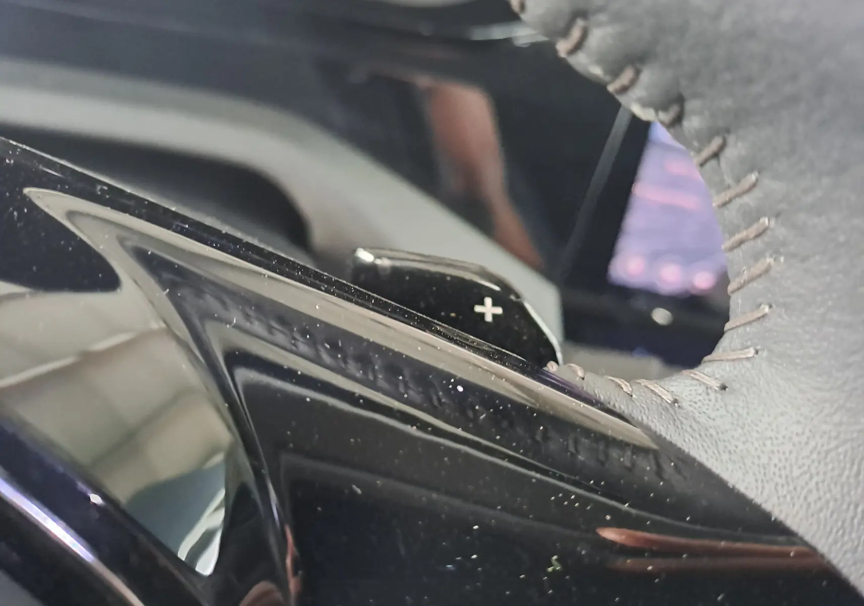 Gros plan sur la palette de changement de vitesse "+" derrière le volant cuir gris du Peugeot 308 Gris Artense 2023.