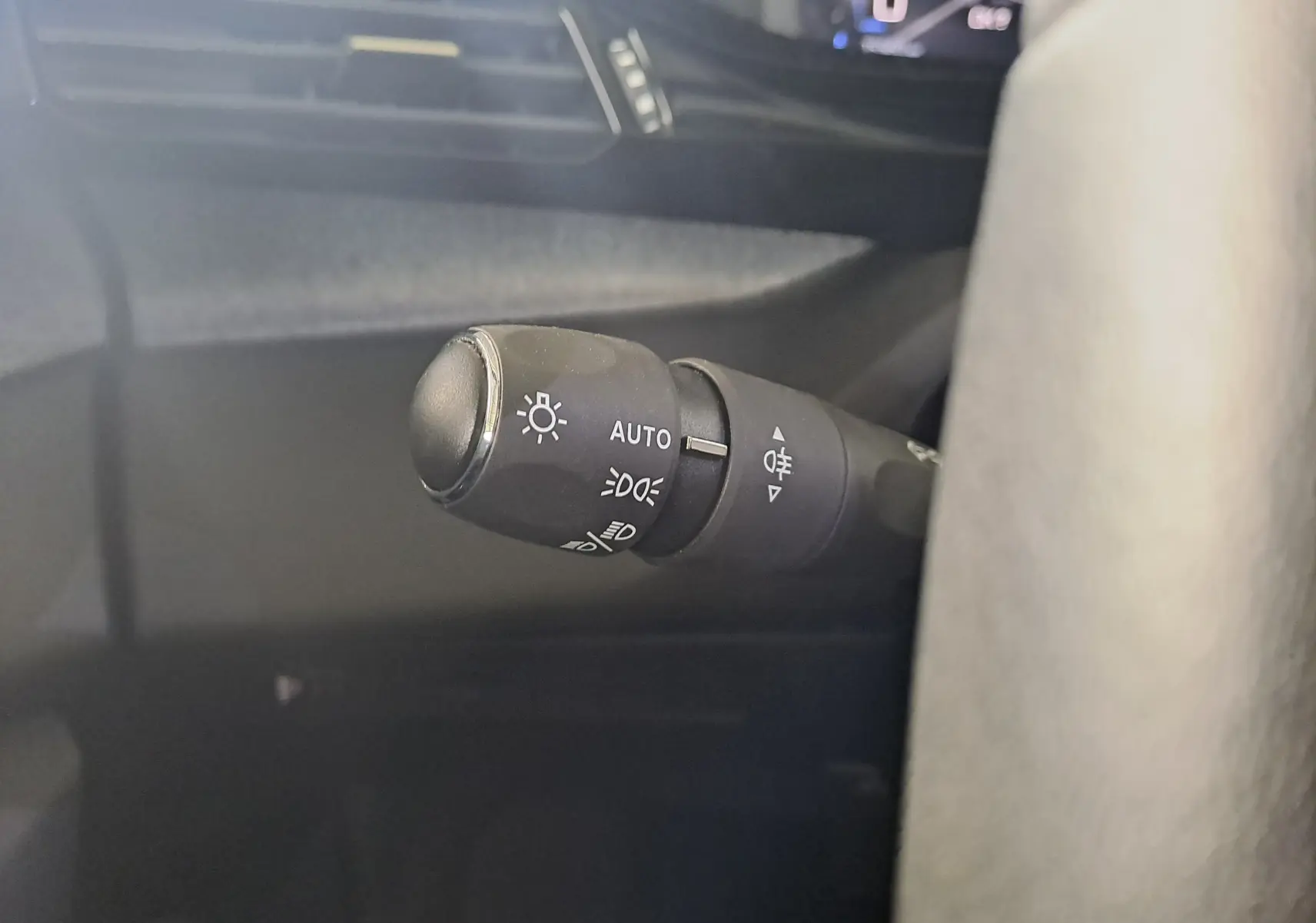 Gros plan sur la commande des feux automatiques à gauche du volant dans l'habitacle d'une Peugeot 308 gris Artense 2023.