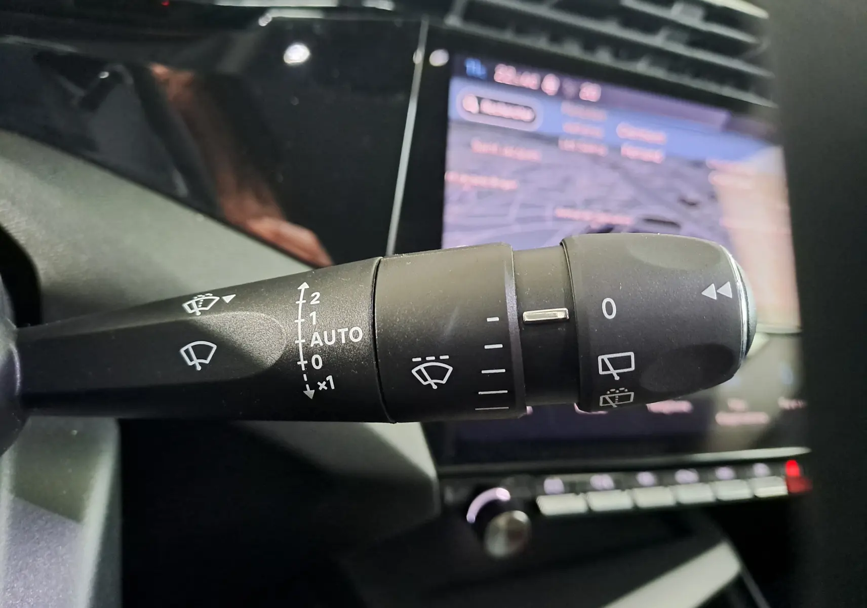 Gros plan sur la commande d'essuie-glace à gauche du volant d'une Peugeot 308 gris Artense 2023, avec écran tactile en arrière-plan.