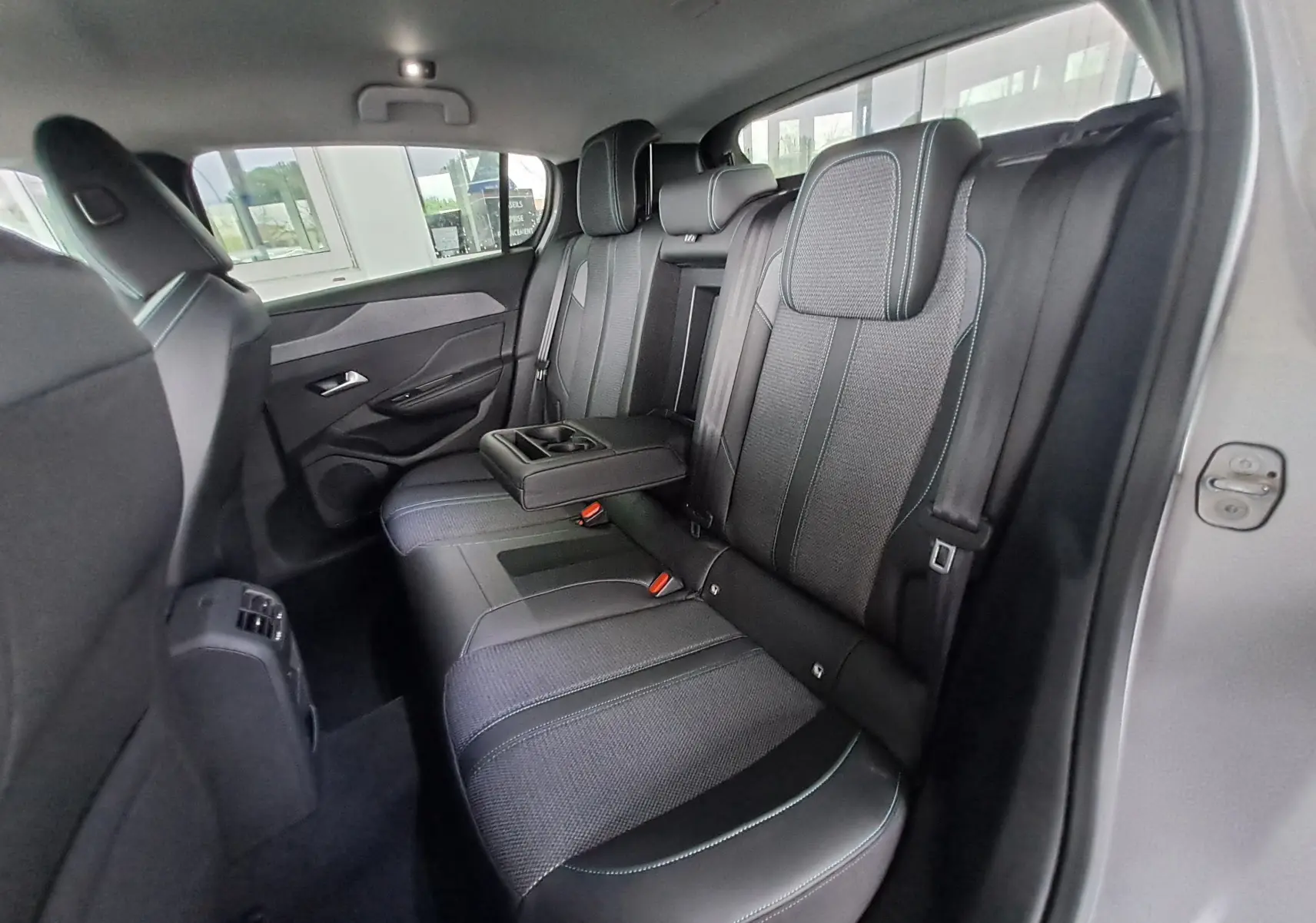 Vue intérieure de la banquette arrière grise de la Peugeot 308 2023 avec accoudoir central relevé et ceintures visibles.