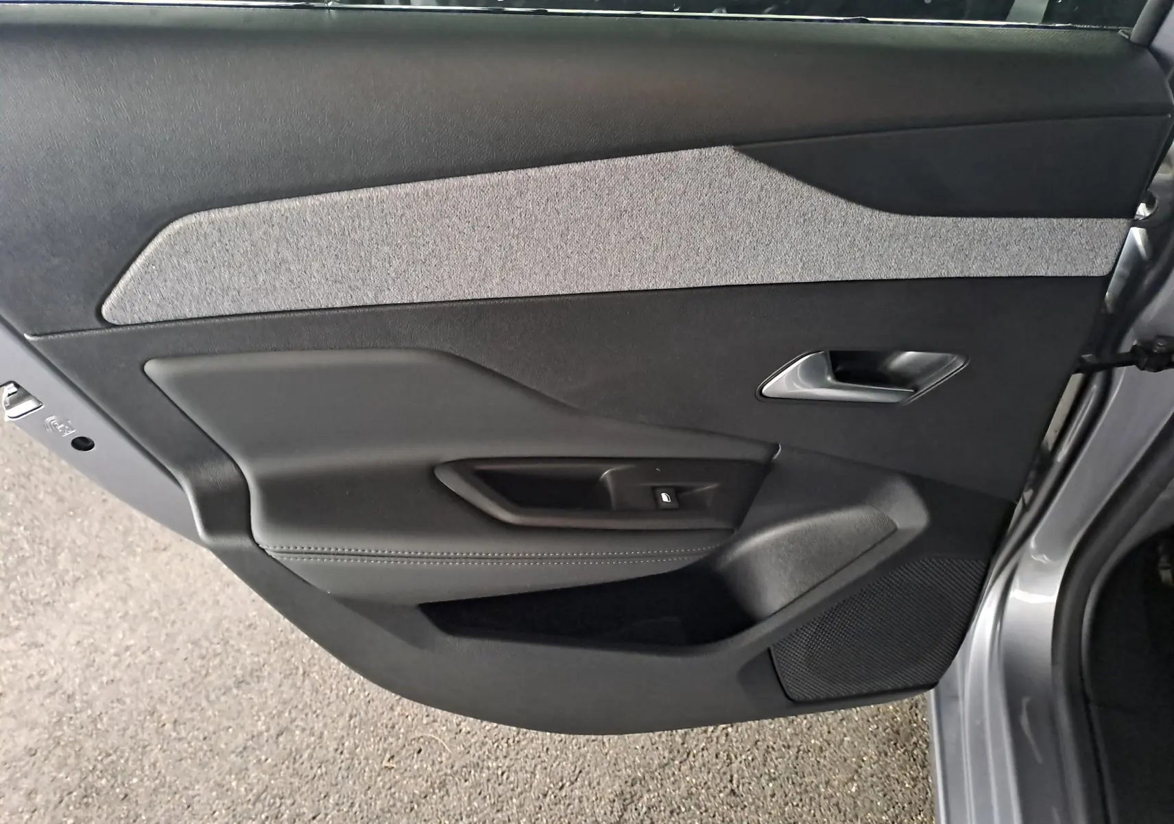 Intérieur de la porte côté gauche d'une Peugeot 308 2023 gris Artense, avec garniture textile grise et poignée argentée.