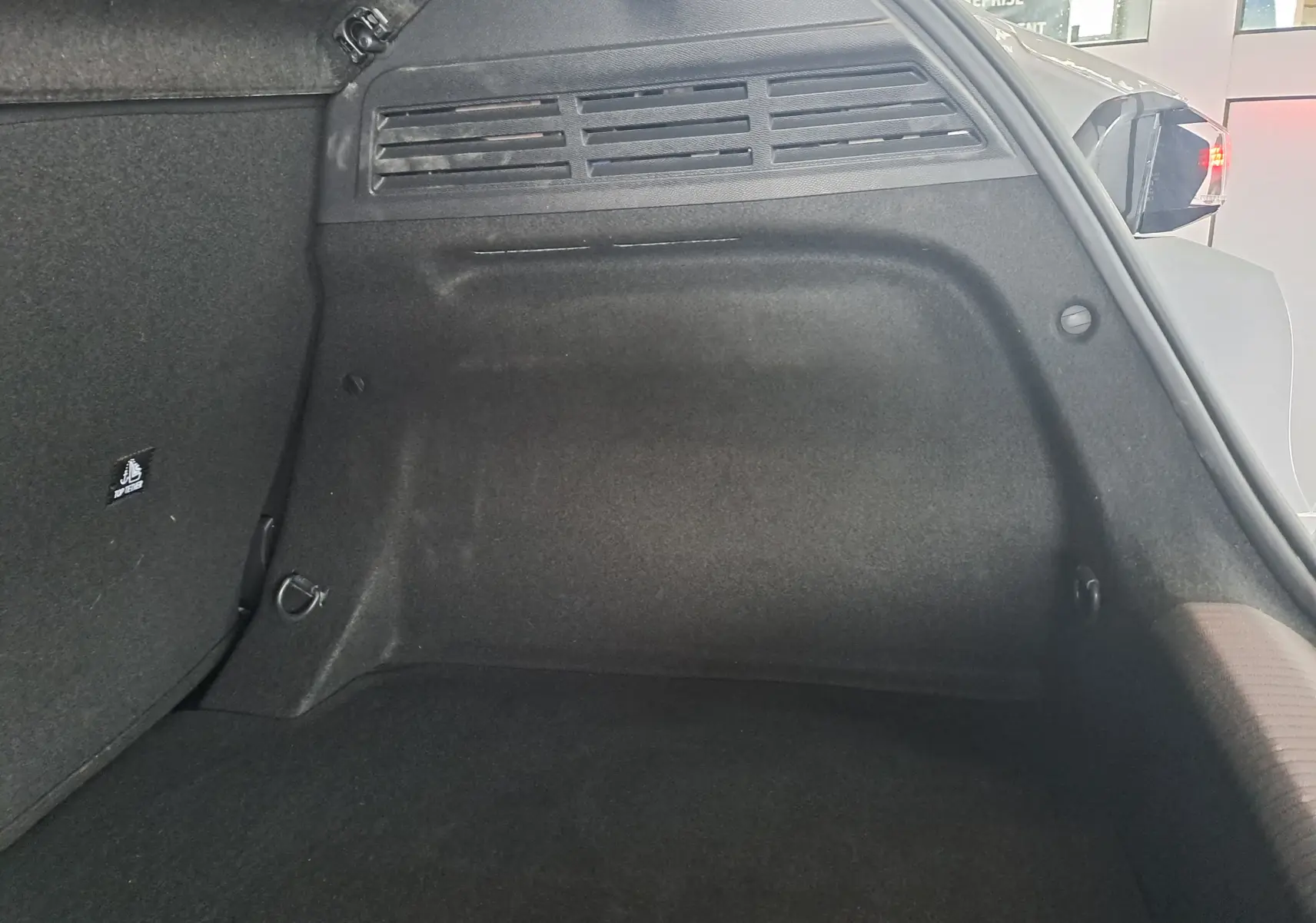 Vue intérieure du coffre arrière droit d'une Peugeot 308 gris Artense, montrant la moquette et les fixations de chargement.