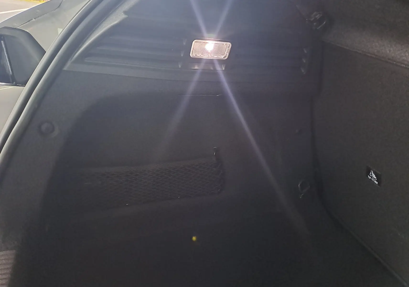 Intérieur du coffre noir d'une Peugeot 308 gris Artense, avec filet de rangement et éclairage allumé côté gauche.