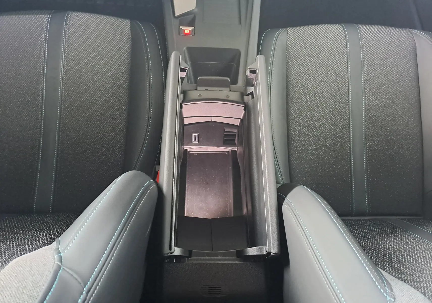 Vue plongeante sur l'accoudoir central ouvert et les sièges avant gris anthracite avec surpiqûres bleues du Peugeot 308 2023.