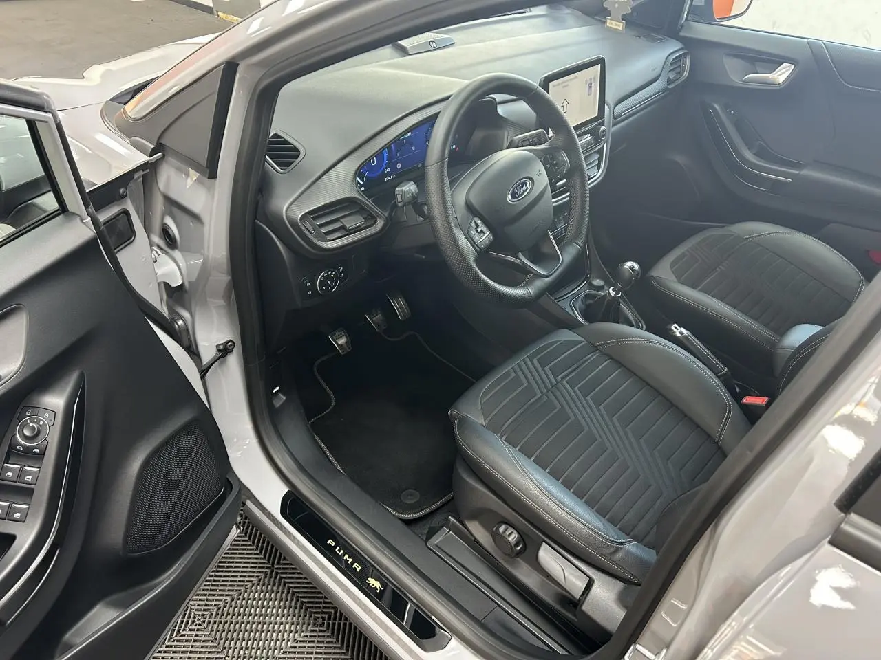 Intérieur côté conducteur du Ford Puma gris 2023, volant multifonction, sièges noirs et écran tactile central visible.