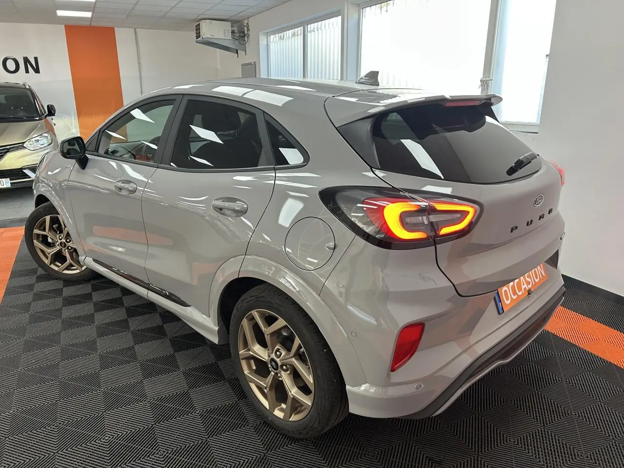 Ford Puma gris métallisé vu de l'arrière droit avec jantes alliage dorées et feux arrière LED allumés.