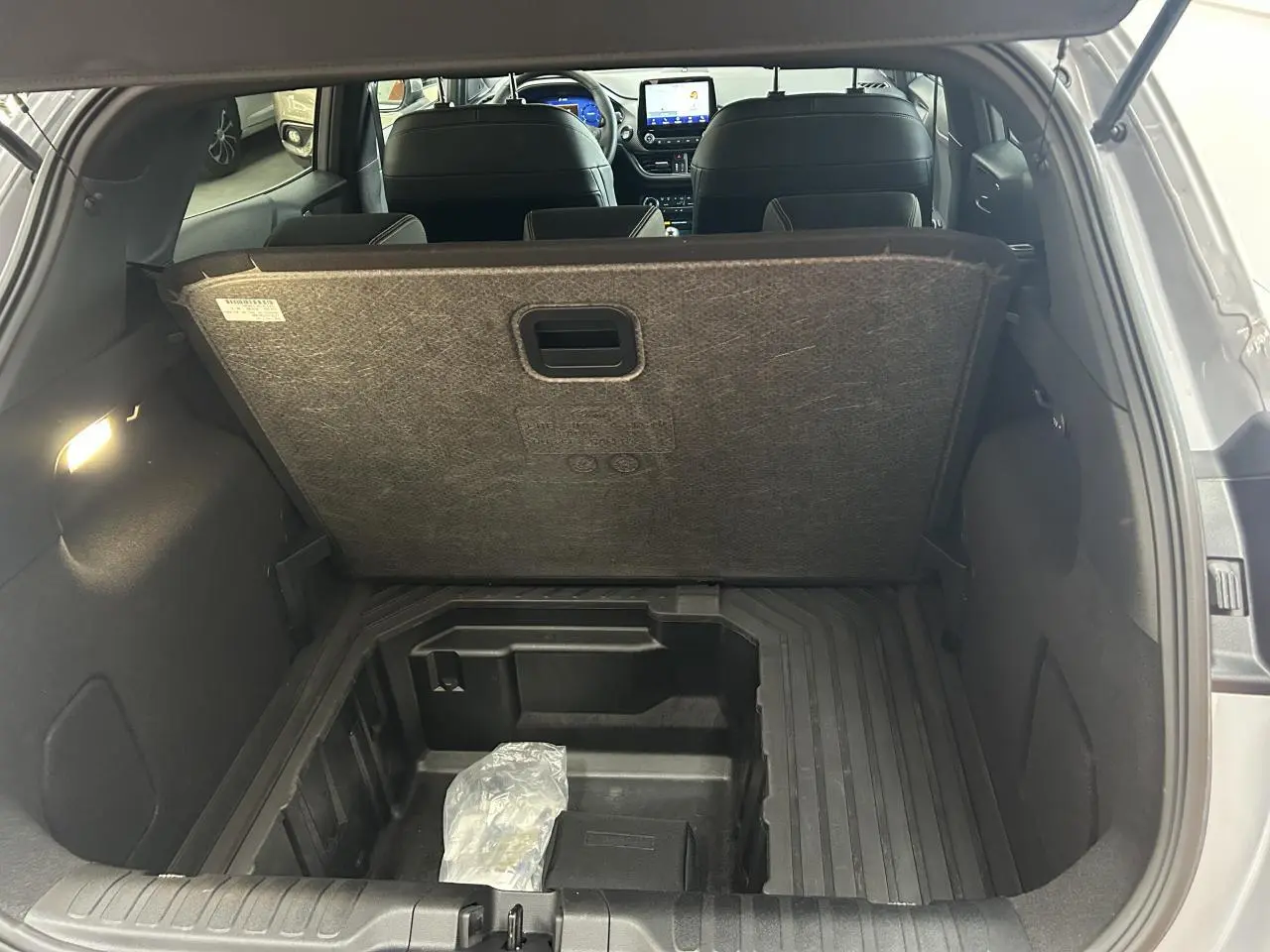 Coffre ouvert vu de l'arrière d'un Ford Puma gris, montrant le compartiment de rangement sous plancher.