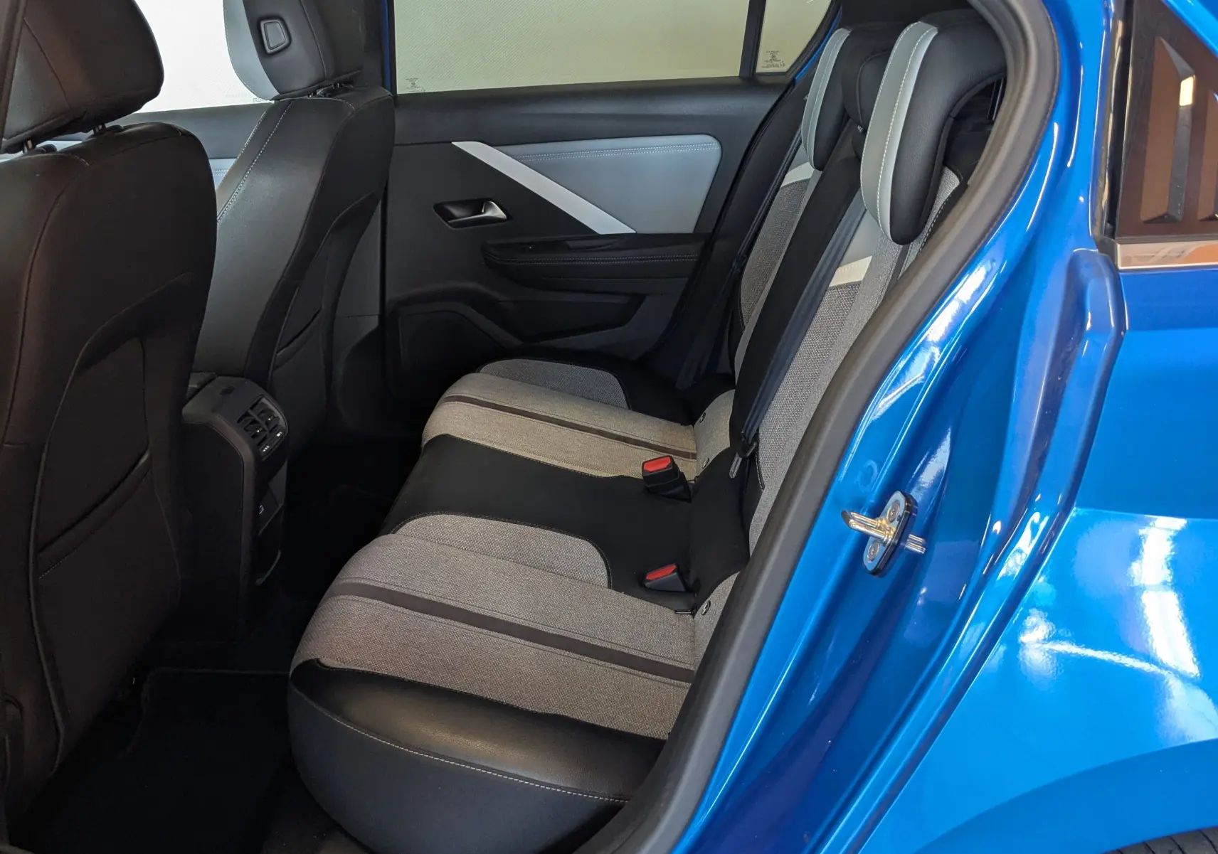 Vue côté gauche arrière de l'intérieur bleu d'une Opel Astra 2022, sièges bicolores gris et noir avec porte ouverte.
