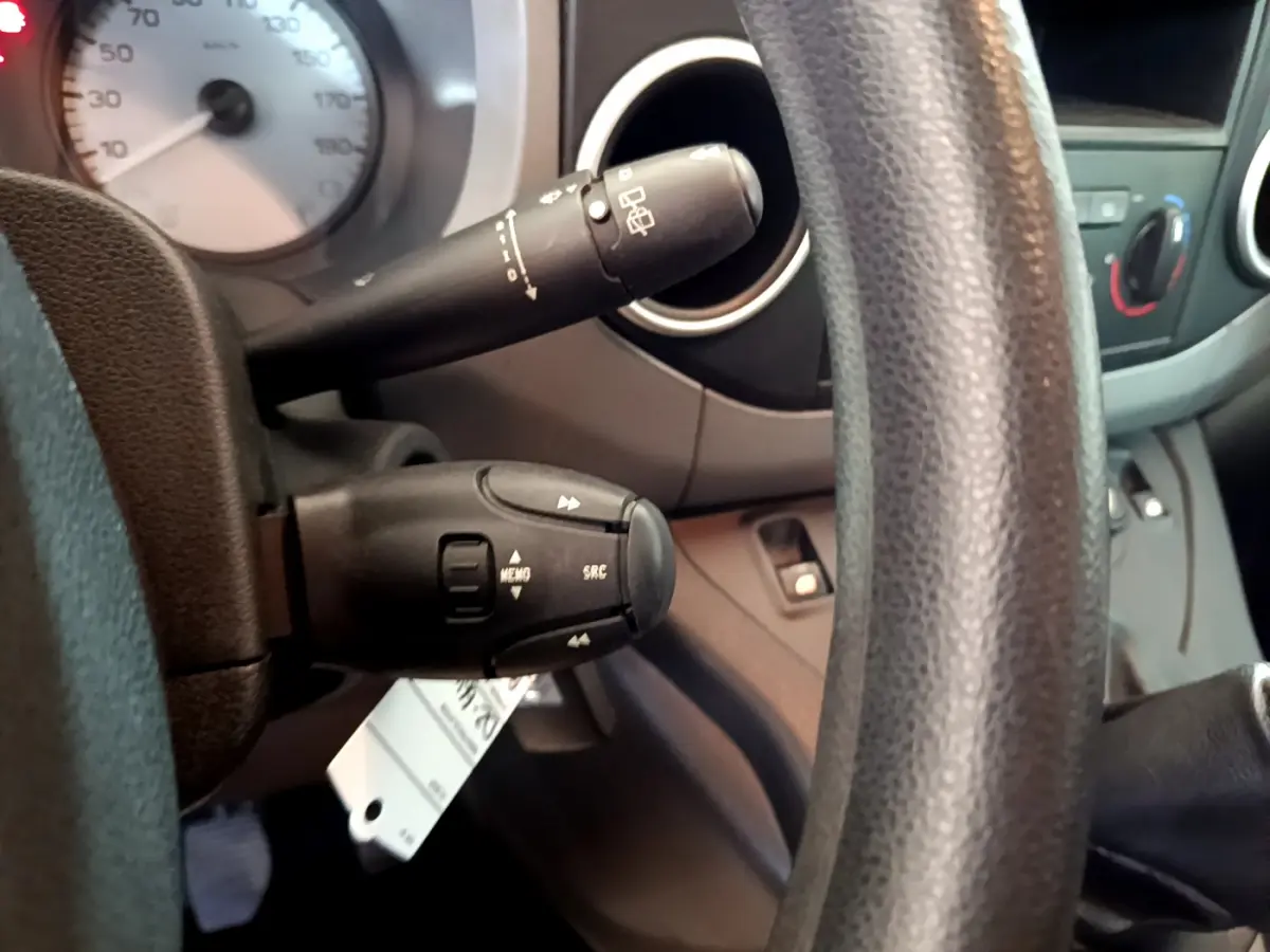 Gros plan sur la colonne de direction et commandes au volant du Citroën Berlingo rouge, tableau de bord en arrière-plan.