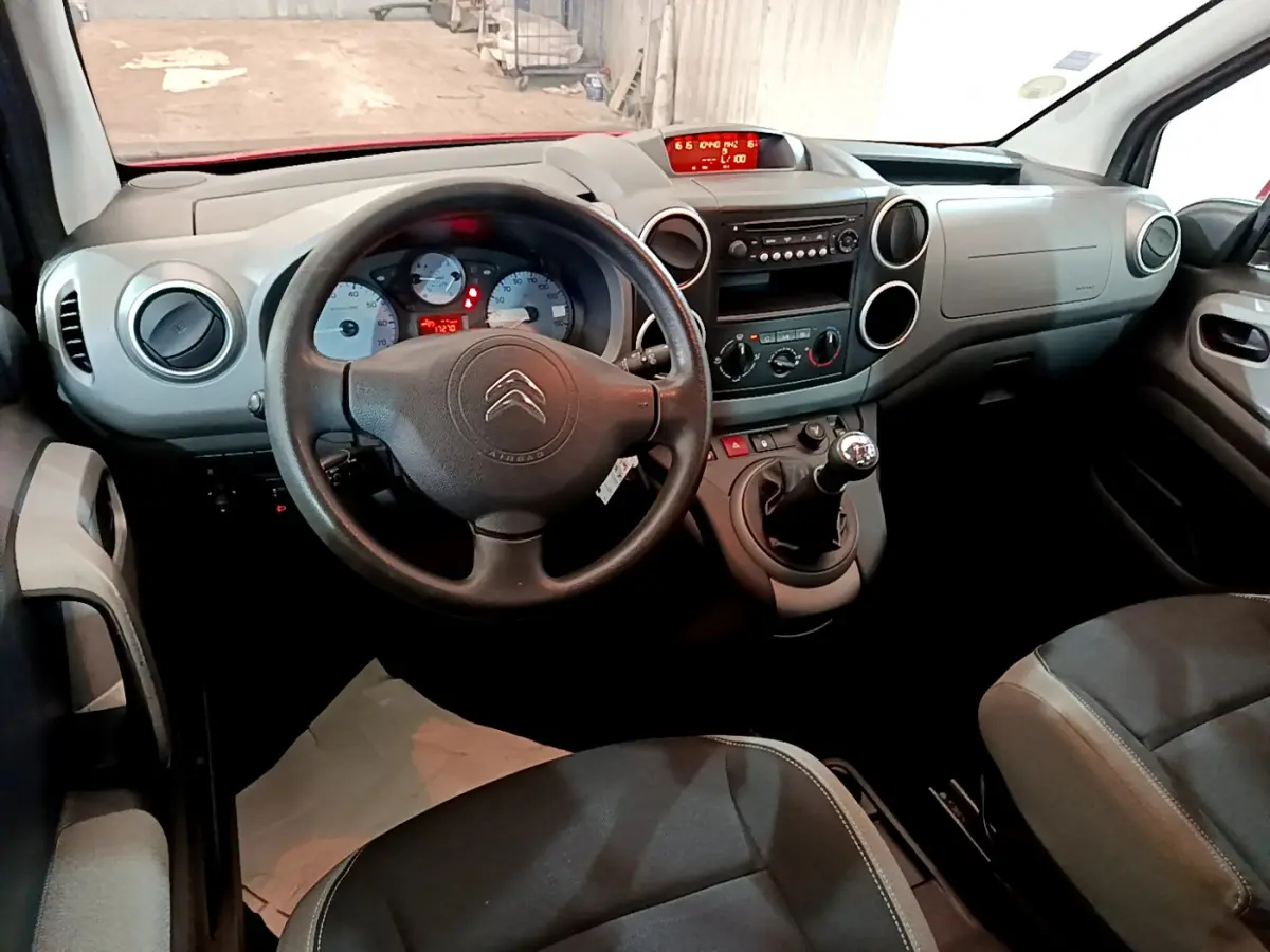 Vue intérieure avant du Citroën Berlingo rouge 2016, volant, tableau de bord et levier de vitesse manuelle visibles.
