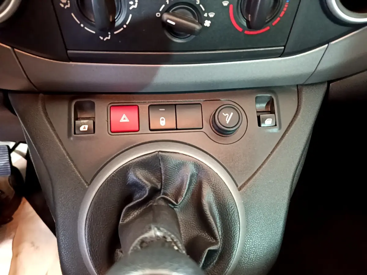 Gros plan sur la console centrale du Citroën Berlingo rouge 2016, montrant la commande de boîte manuelle et les boutons de verrouillage et warning.