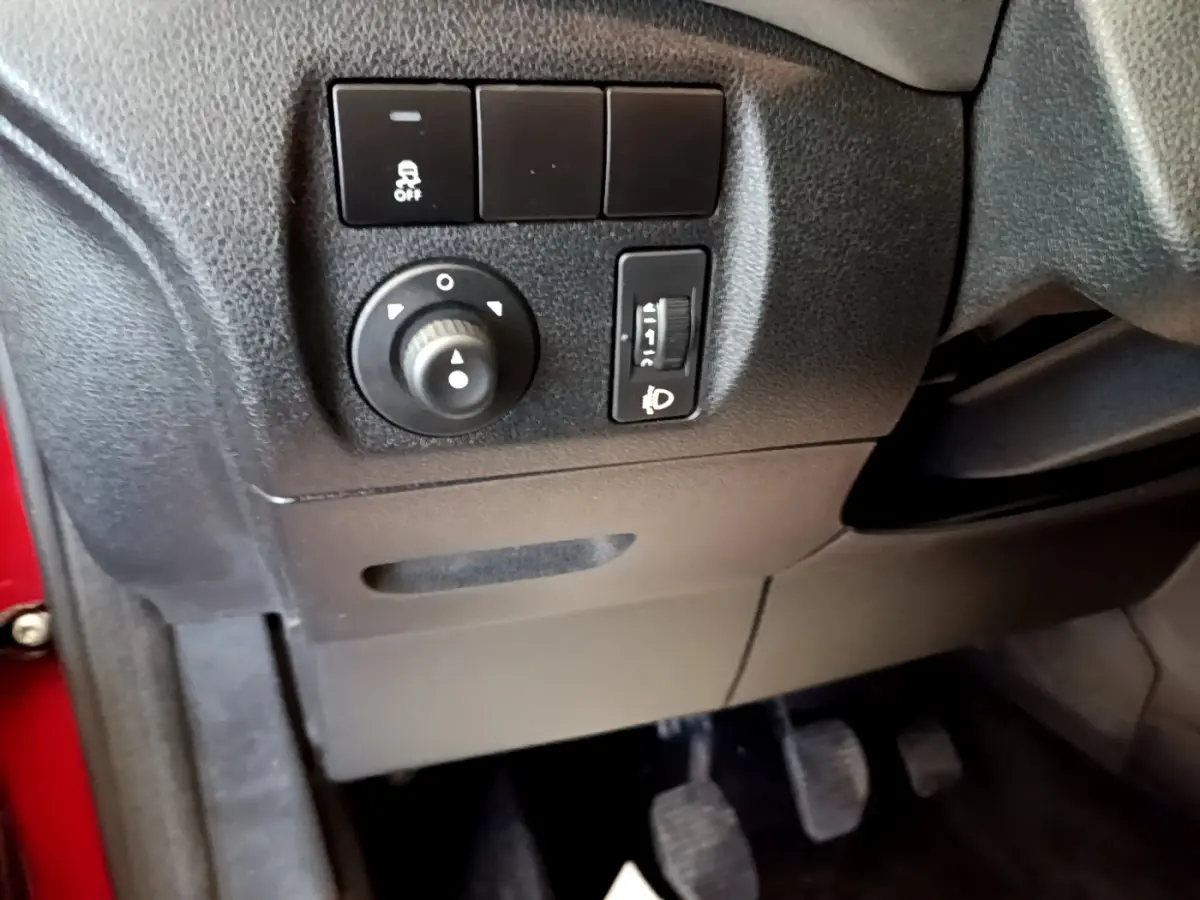 Détail intérieur côté gauche du tableau de bord noir avec commandes de réglage des phares et antipatinage sur Citroën Berlingo rouge.