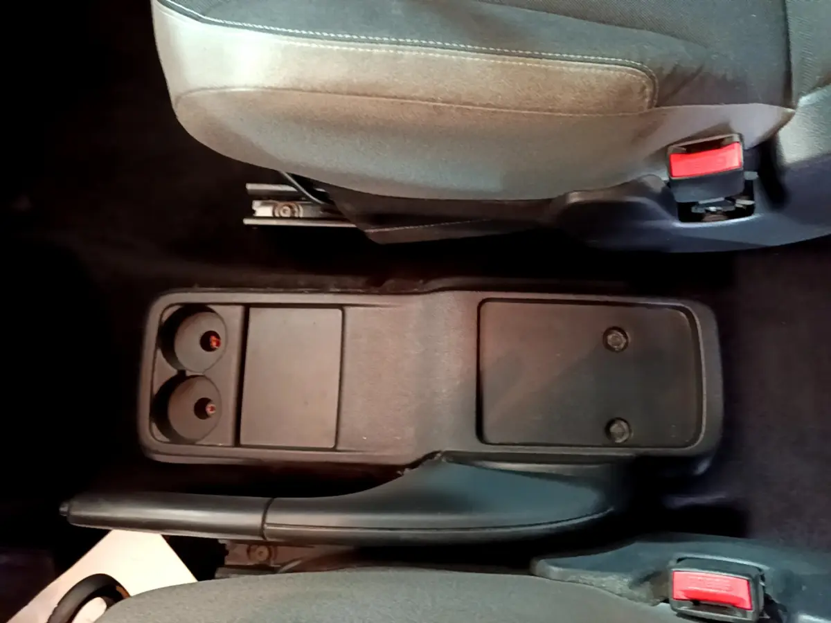Vue plongeante sur la console centrale noire et frein à main entre les sièges avant gris du Citroën Berlingo rouge 2016.
