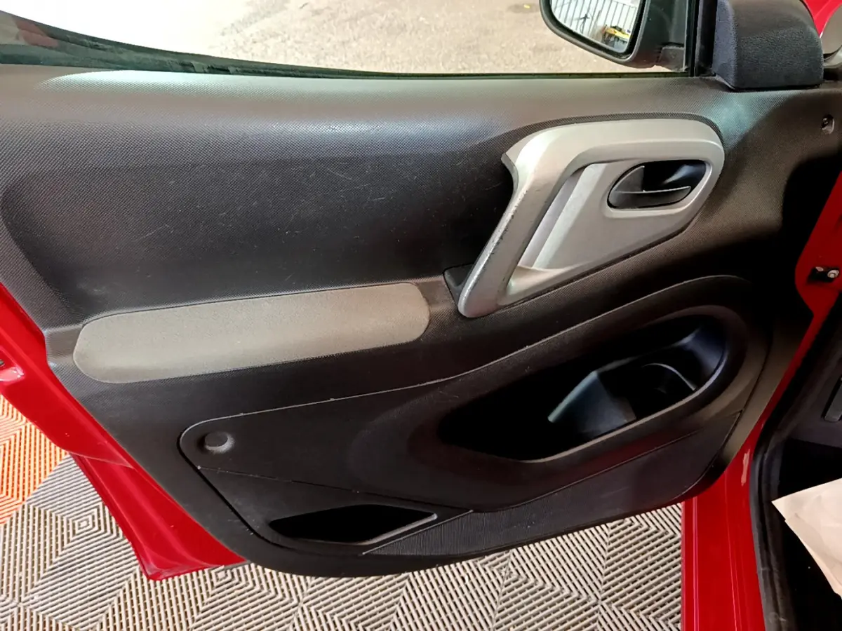 Gros plan sur la porte avant gauche rouge du Citroën Berlingo 2016, montrant la poignée intérieure et les rangements noirs.