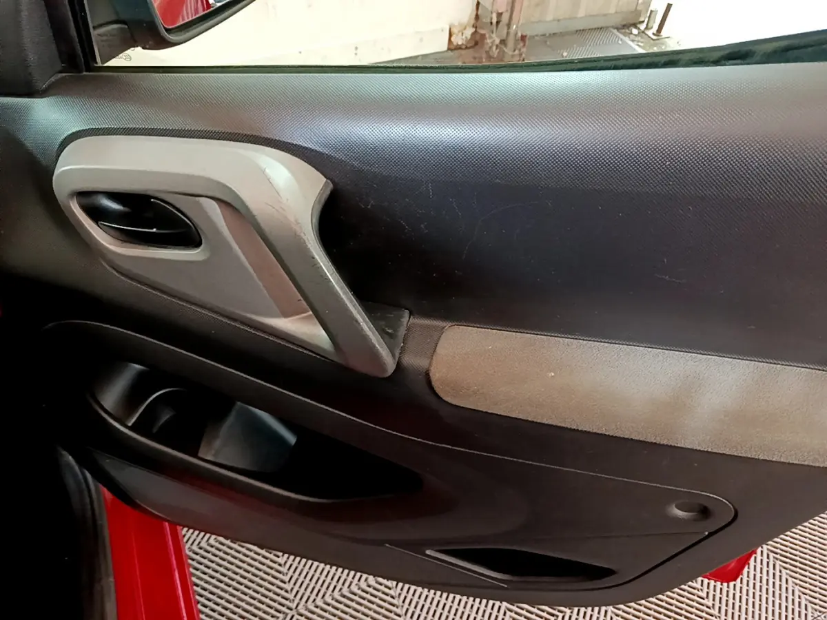 Détail de la porte intérieure côté conducteur du Citroën Berlingo rouge 2016 avec poignée grise et accoudoir noir.