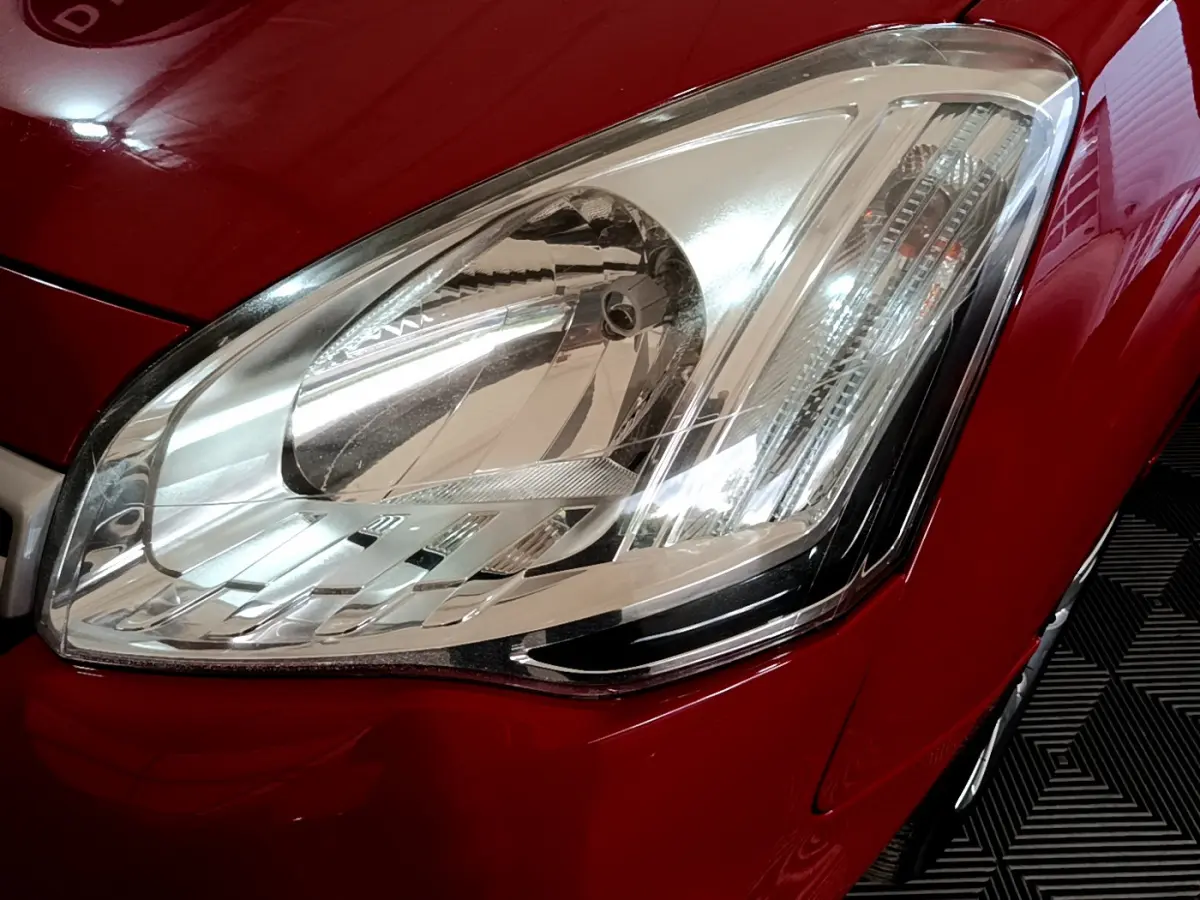 Gros plan sur le phare avant droit d'un Citroën Berlingo rouge 2016, mettant en valeur la finition lumineuse détaillée.