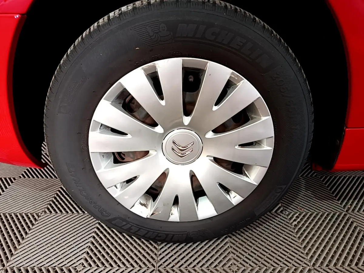 Gros plan sur la roue avant gauche du Citroën Berlingo rouge de 2016 avec enjoliveur argenté et pneu Michelin.
