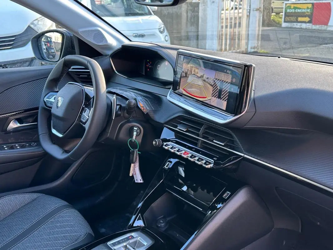 Vue intérieure côté conducteur du tableau de bord noir de la Peugeot 208 Hybrid 110 avec écran tactile et volant multifonction.