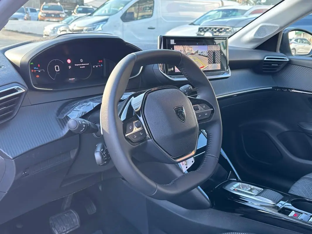 Vue intérieure de face du volant et du cockpit numérique de la Peugeot 208 Hybrid 110 Allure blanche avec écran tactile central.