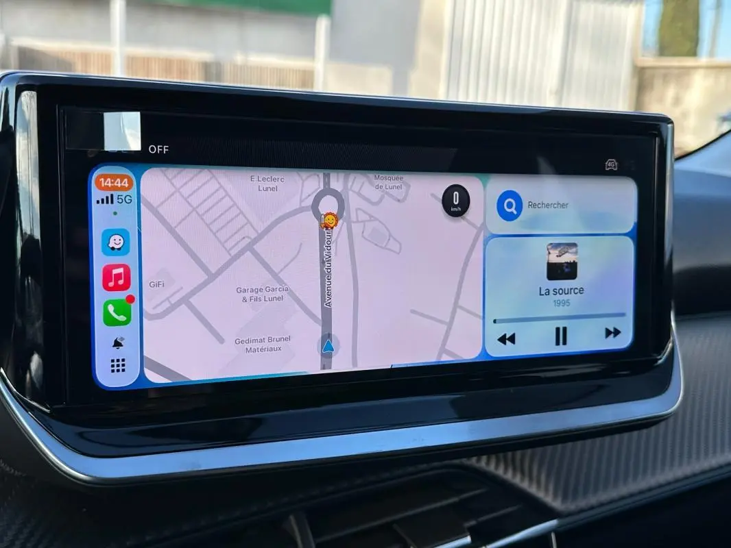 Écran tactile du tableau de bord de la Peugeot 208 blanc, affichant navigation et musique en vue rapprochée.