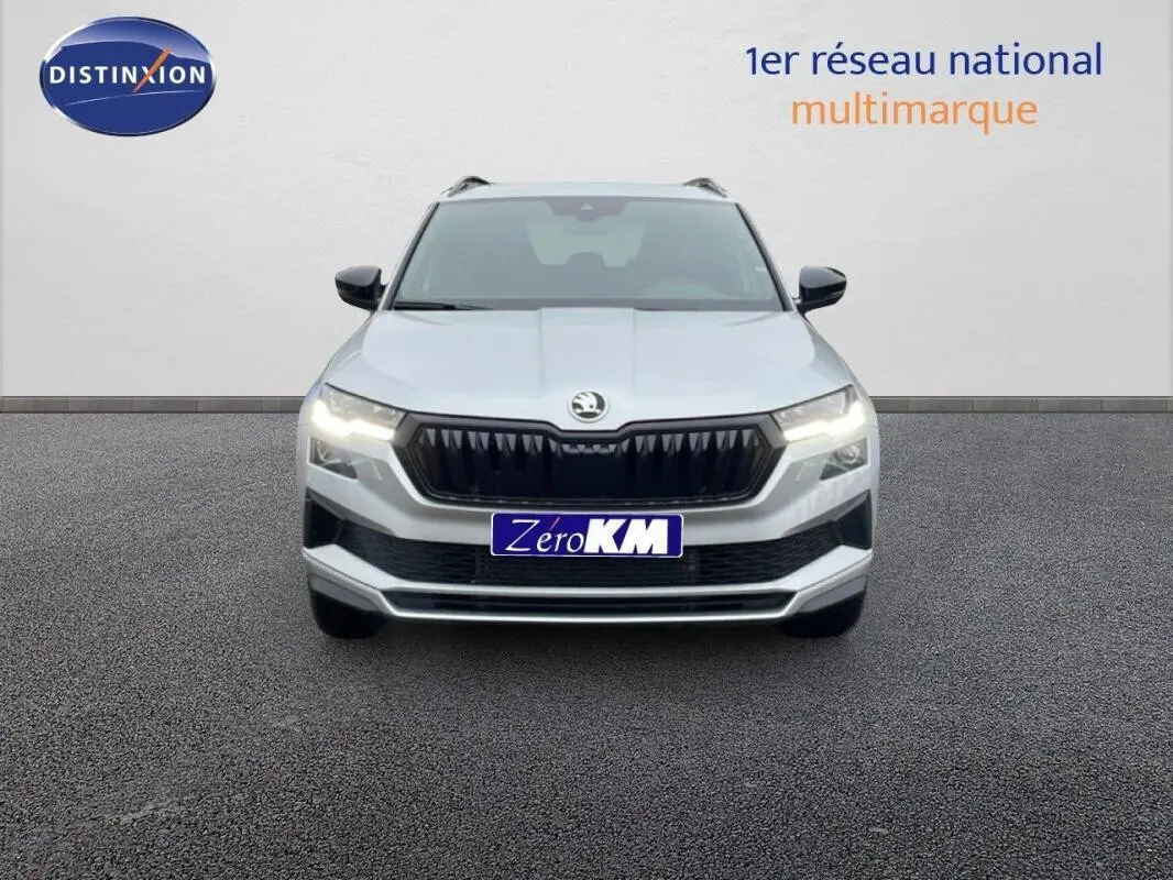 Vue frontale d'un Skoda Karoq argent 2025 avec calandre noire et phares allumés sur fond neutre.
